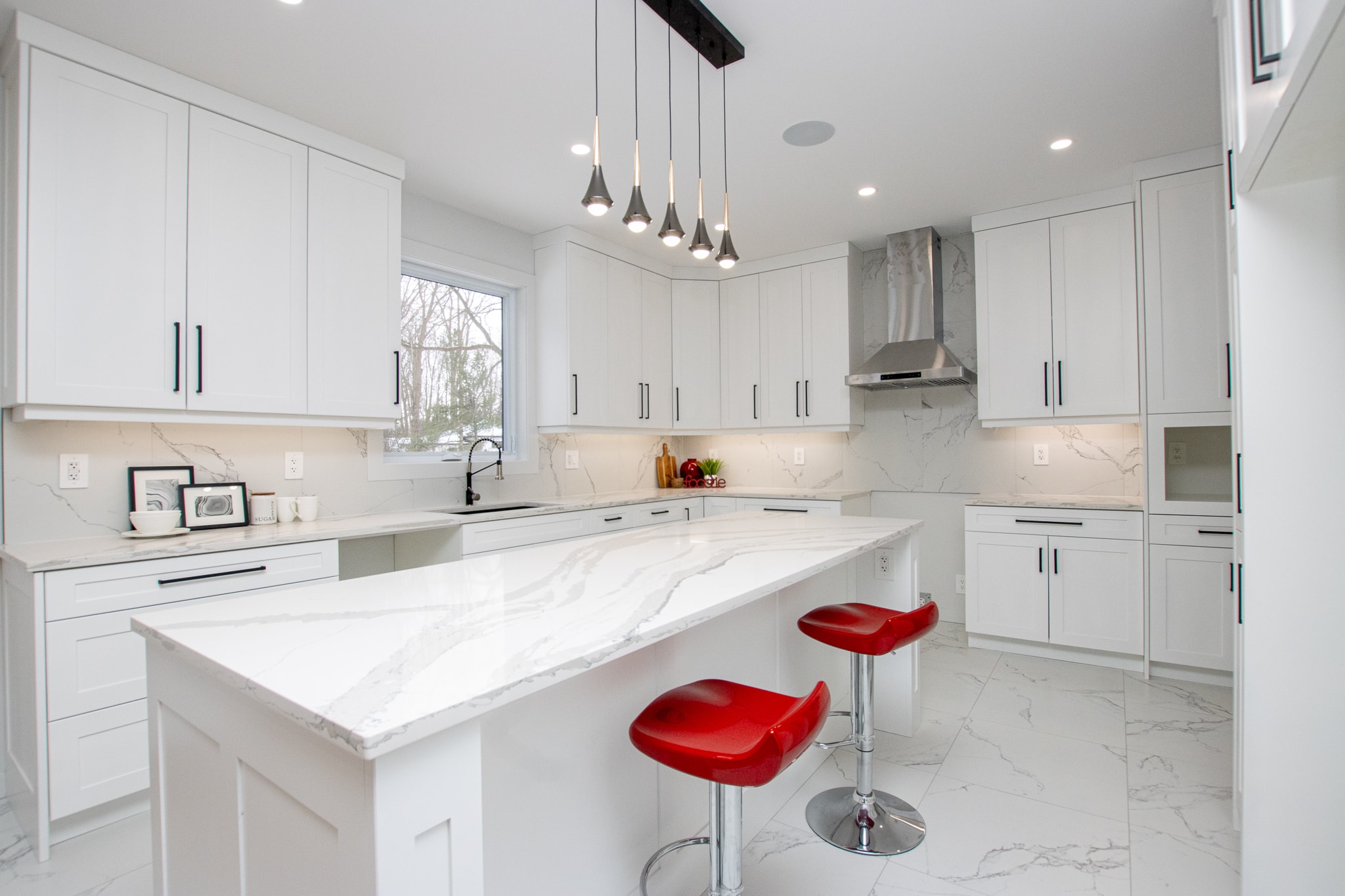 White kitchen with marble countertops and red bar stools